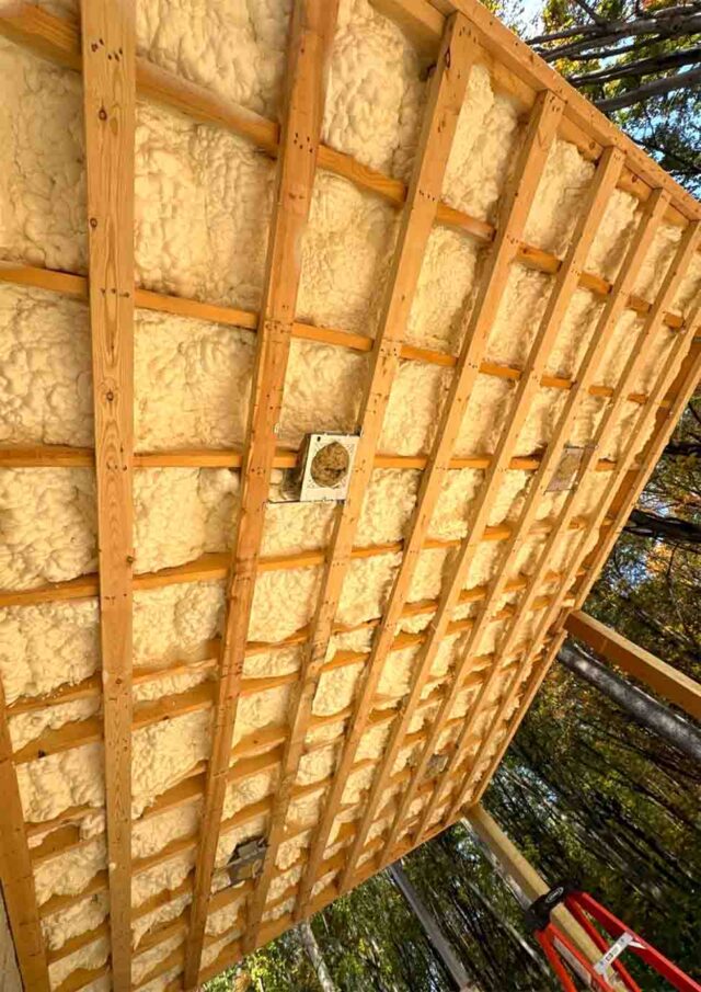 Foam InSEALators closed-cell spray foam insulation applied between floor joists on the underside of an elevated exterior cold floor, with wood strapping and electrical boxes visible.