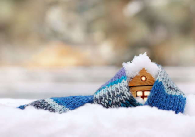 Wood house model in the snow, wrapped in a blue knitted scarf.
