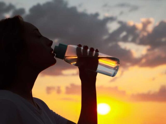 Silhouette of woman drinking water from a glass bottle at sunrise or sunset.