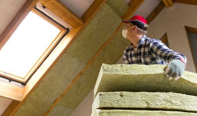Worker installing mineral wool insulation in a vaulted ceiling with a window.