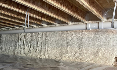 Closed-cell spray foam insulation applied to crawl space foundation wall with vapor barrier installed over the ground.