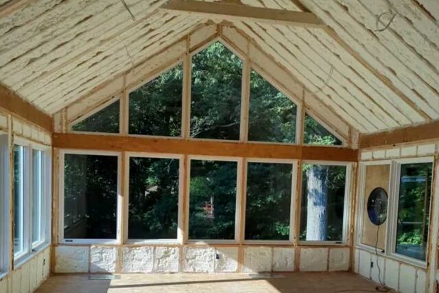 A sunroom under construction with spray foam insulation and large windows.